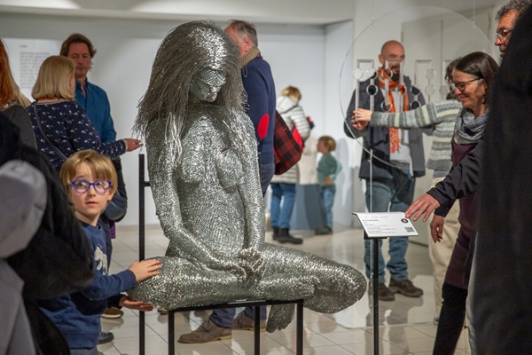 A tactile figure of a seated women surrounded by visitors.